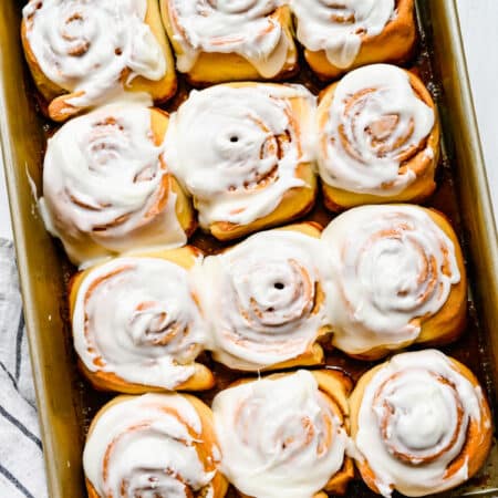 A dozen honey buns with frosting in a pan.