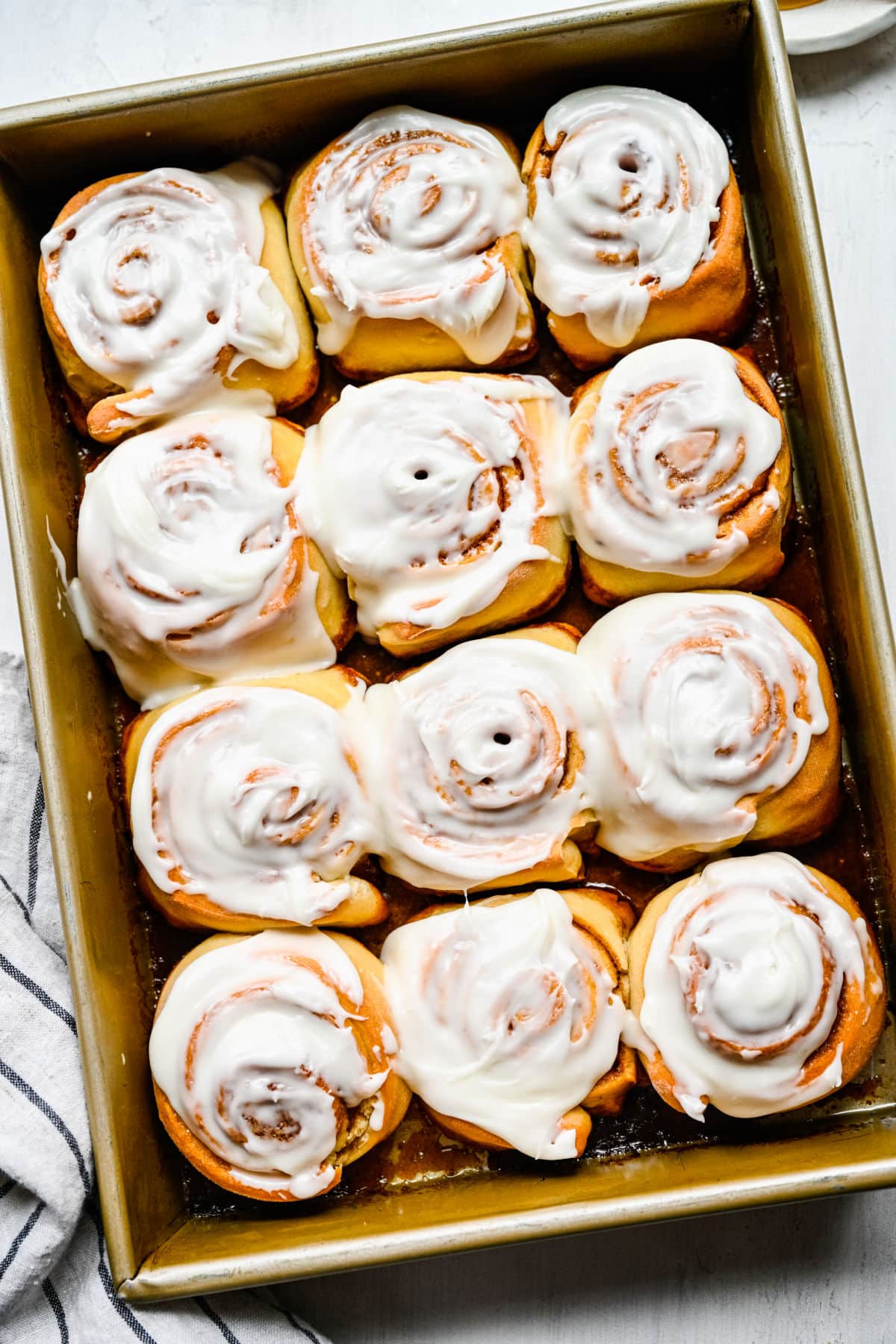 A dozen honey buns with frosting in a pan. 