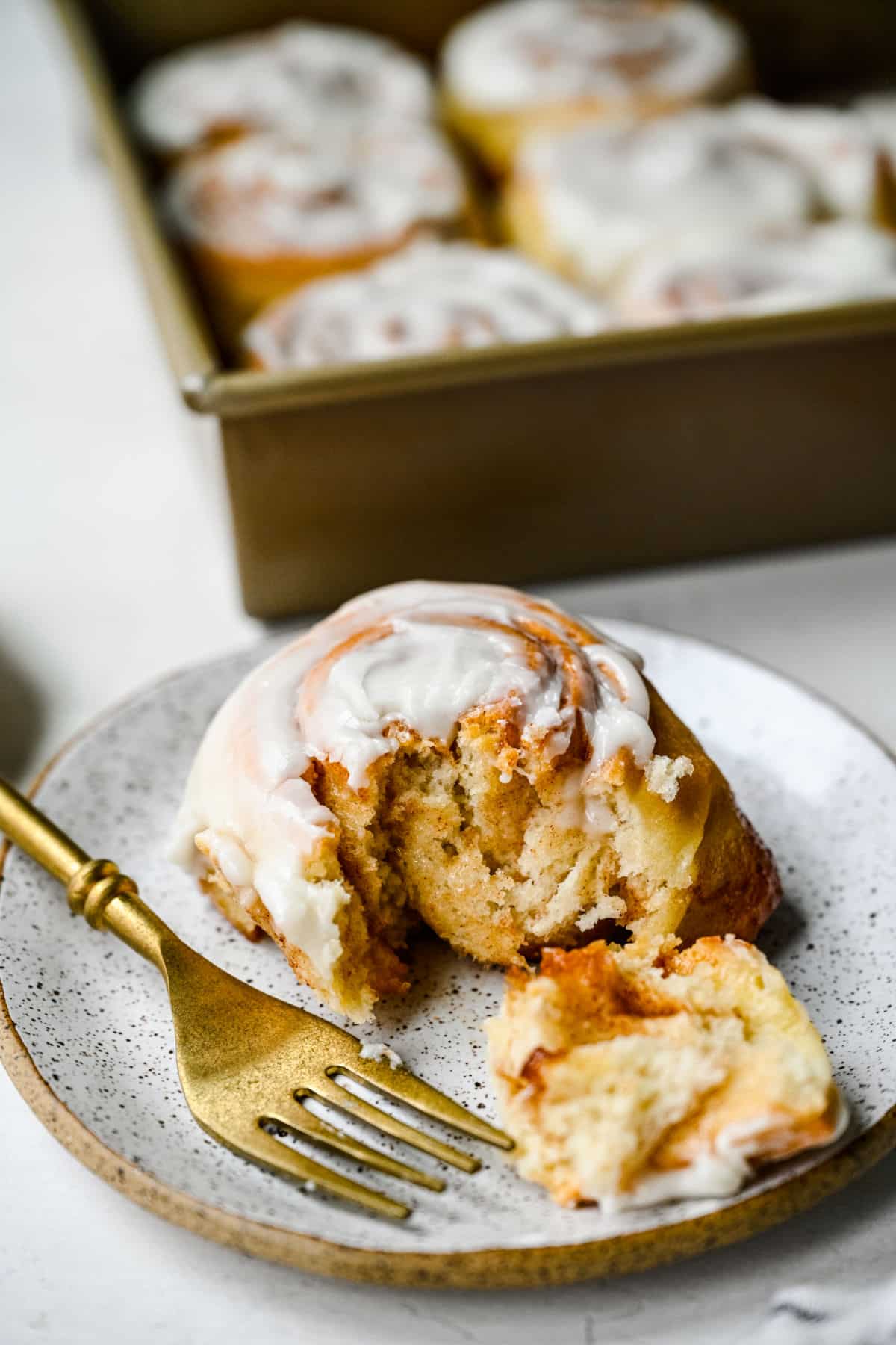 A gold fork taking a bite of a homemade honey bun. 