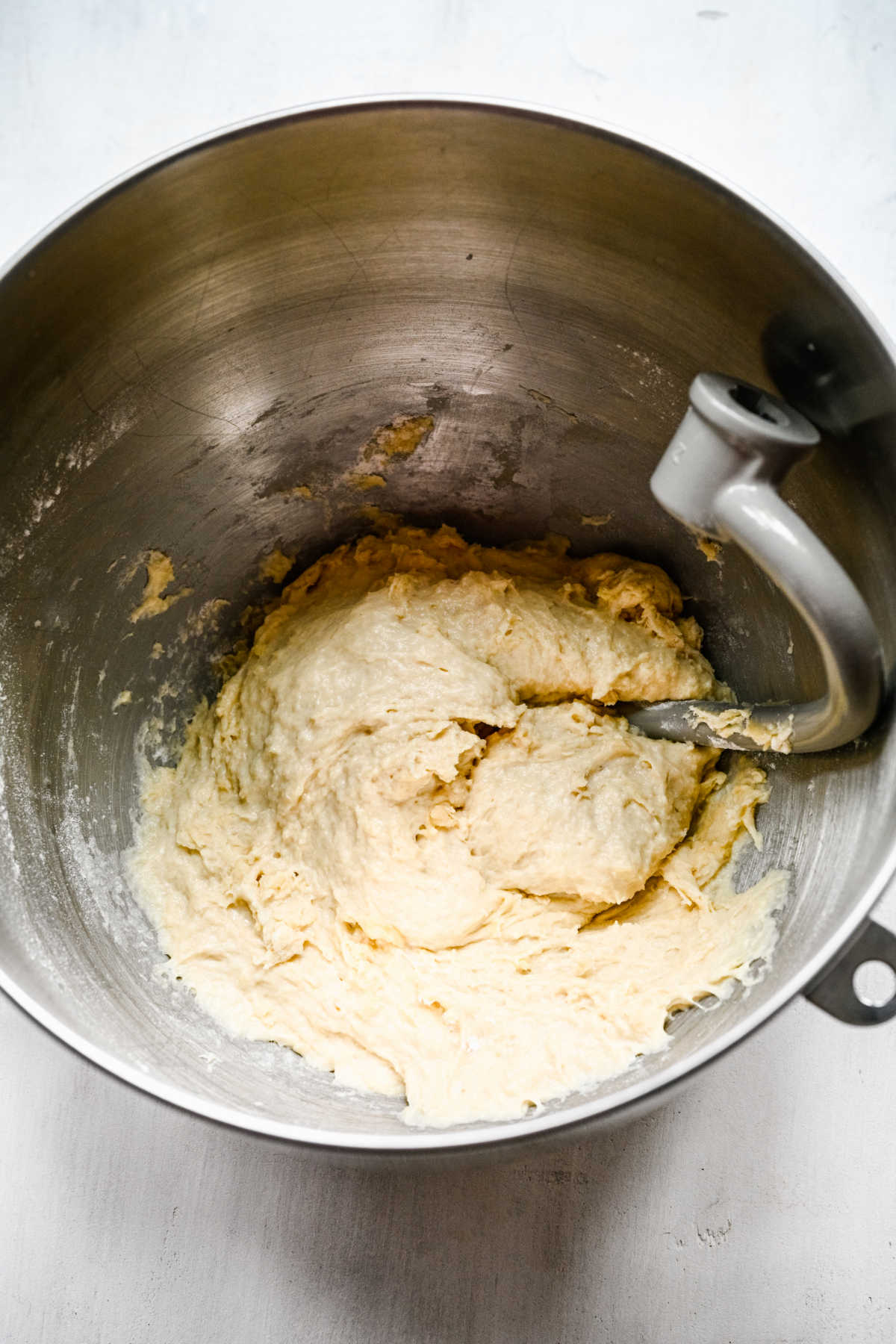 Dough and a dough hook in a silver mixing bowl. 