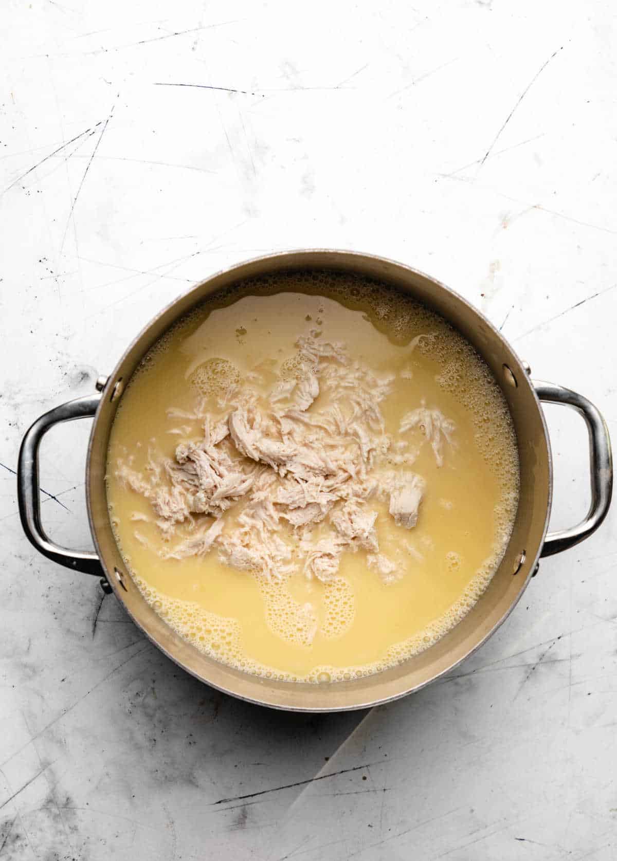 Cooked shredded chicken in a pot of broth.