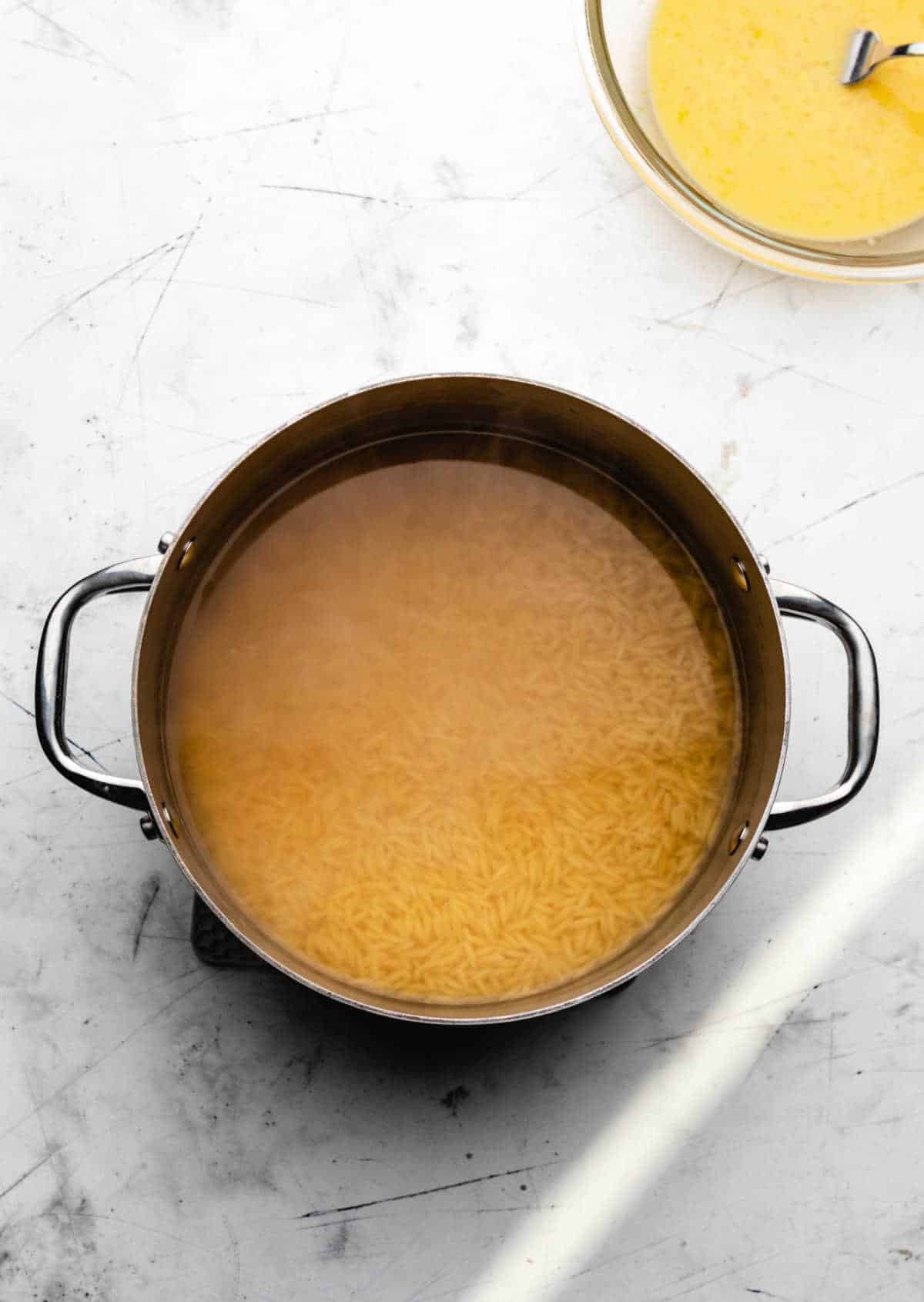 Orzo in chicken broth in a stock pot.