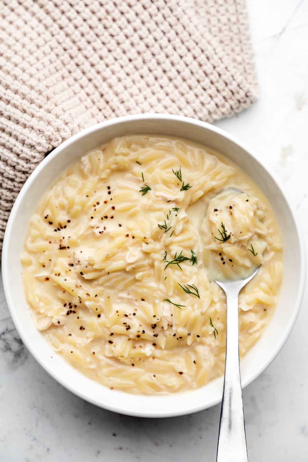 A bowl of avgolemono topped with fresh dill and black pepper.