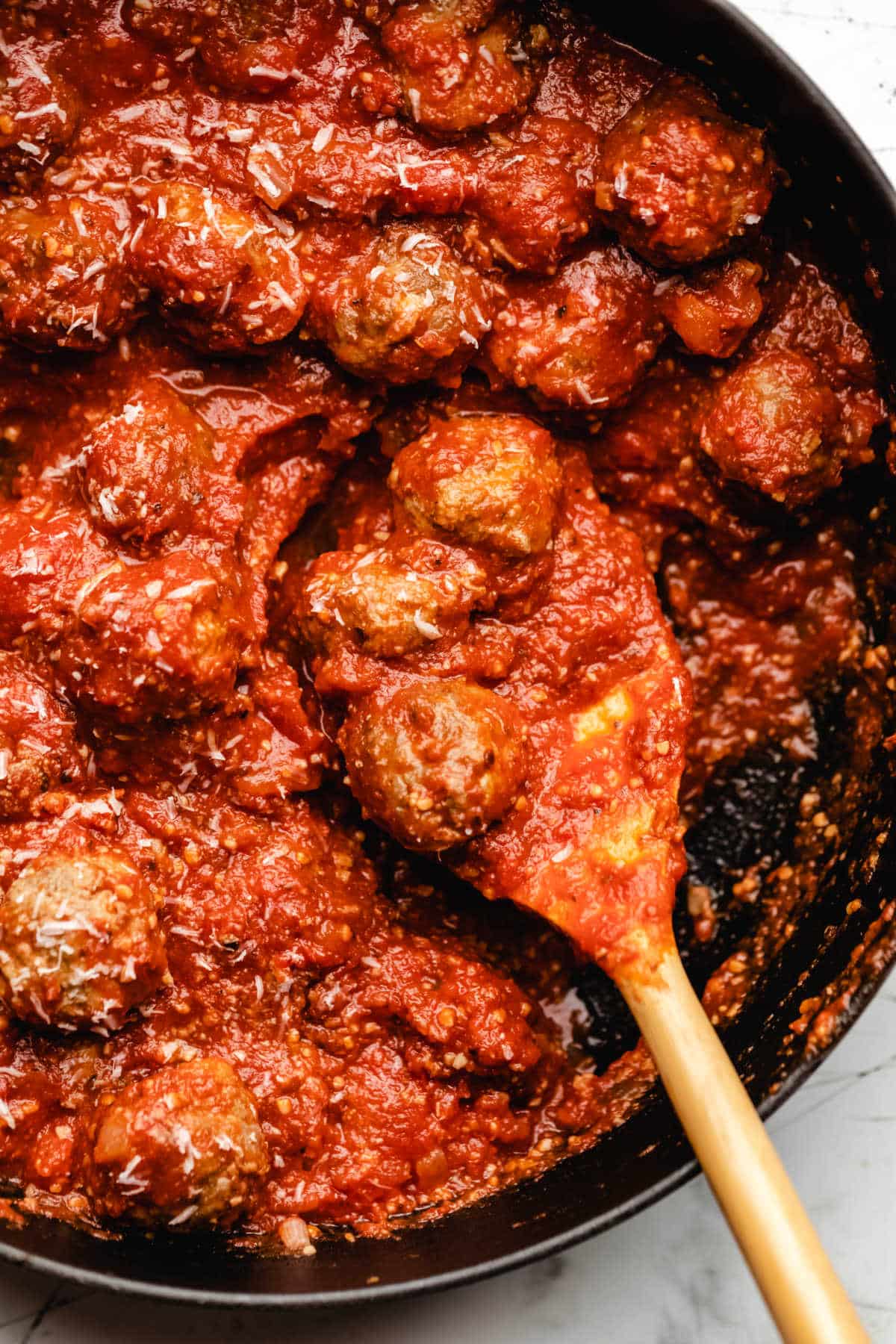 A wooden spoon holding 3 meatballs and sauce. 