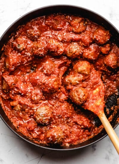 A wooden spoon scooping up 3 baked meatballs in sauce.