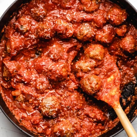 A wooden spoon scooping up 3 baked meatballs in sauce.
