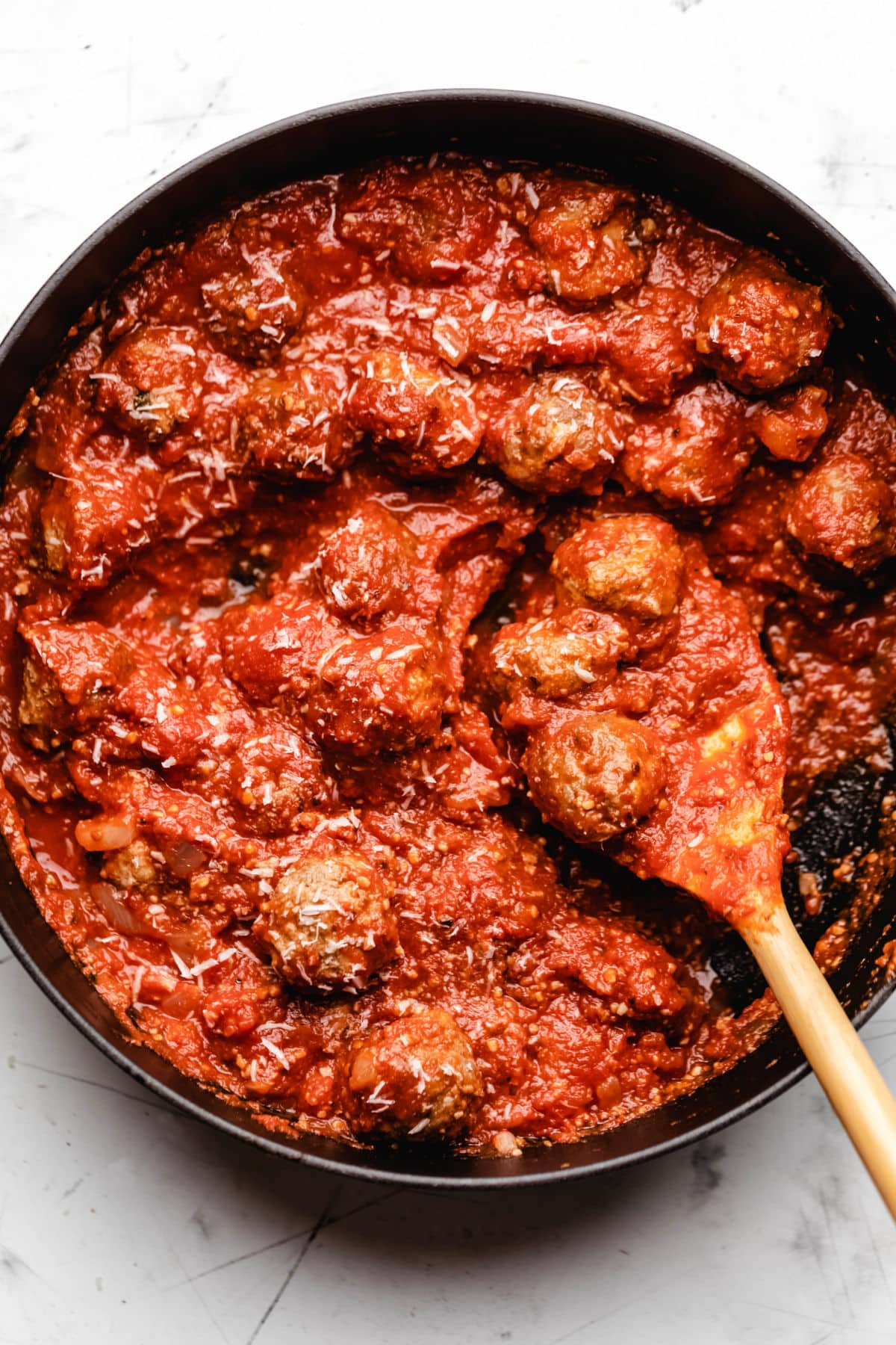 A wooden spoon scooping up 3 baked meatballs in sauce. 