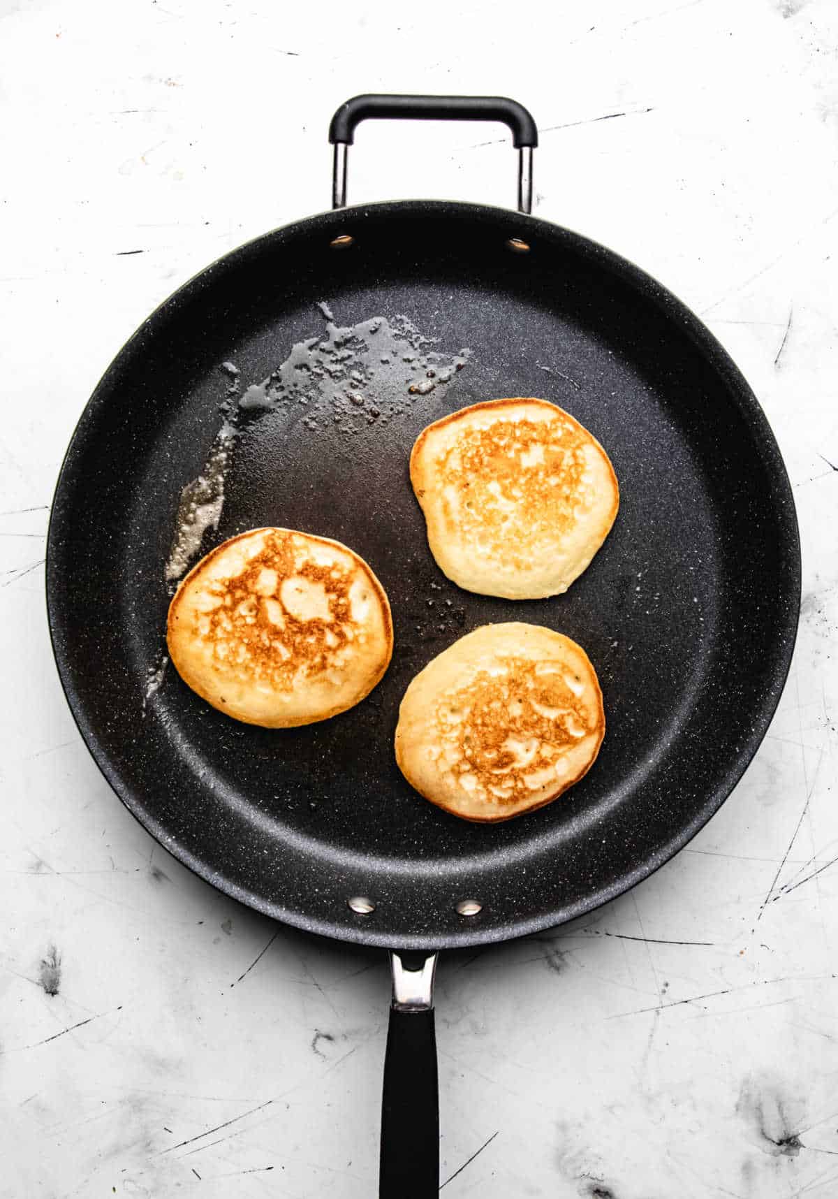 Three pancakes cooking in a skillet. 