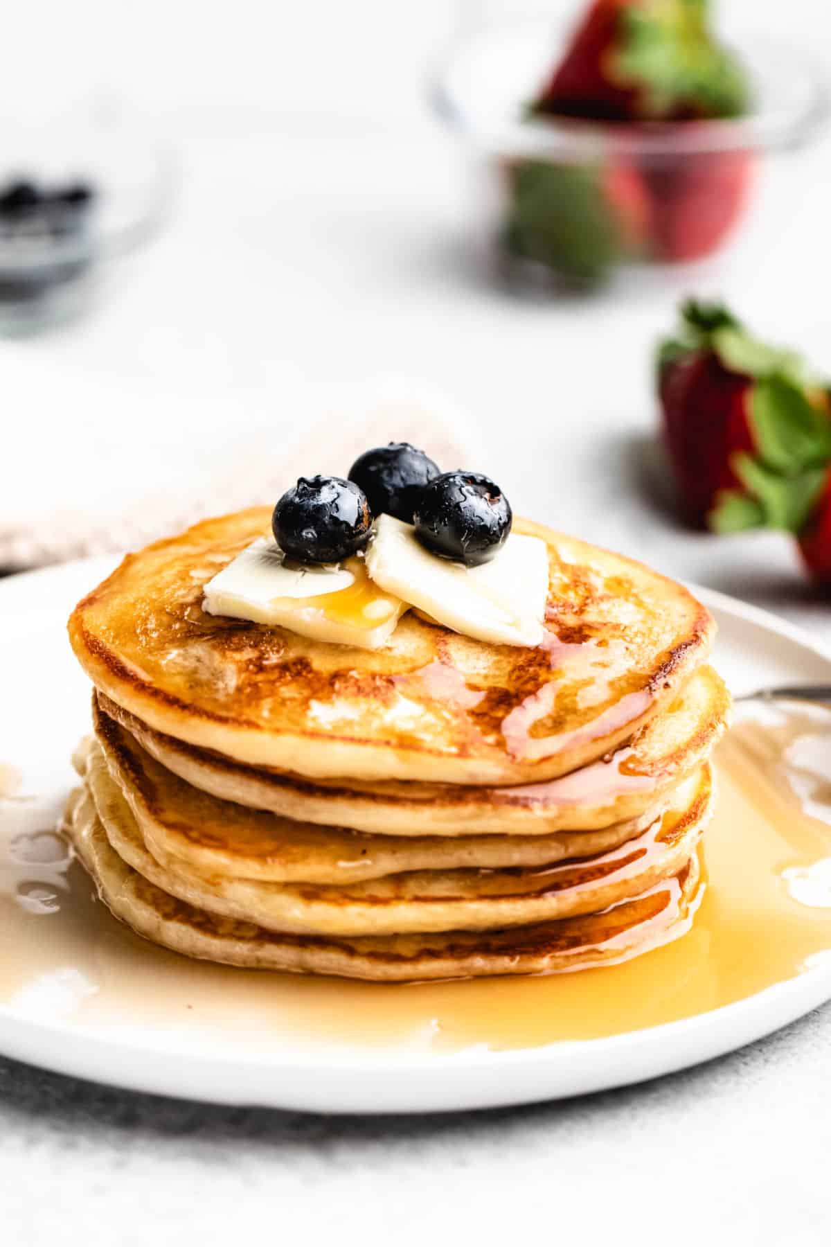 A stack of buttermilk pancakes topped with 3 blueberries butter and syrup.