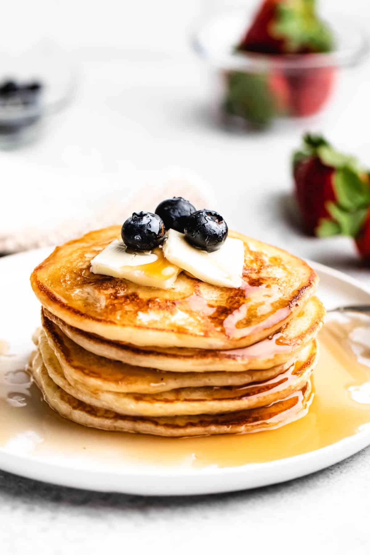 A stack of buttermilk pancakes topped with 3 blueberries butter and syrup. 