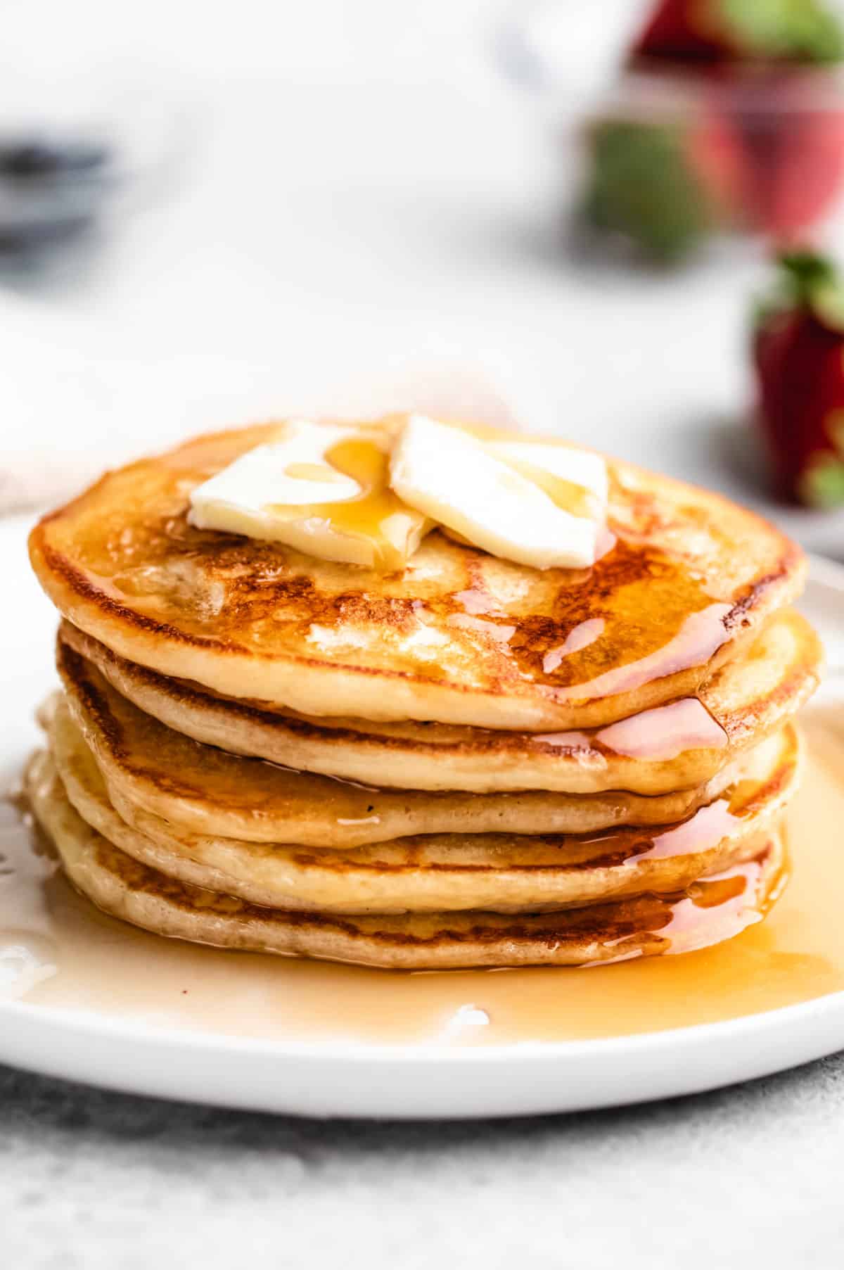 A stack of buttermilk pancakes on a white plate with butter and syrup on them. 