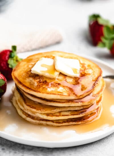 A stack of buttermilk pancakes next to fresh strawberries.