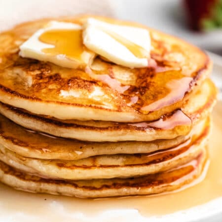 Close up photo of a stack of buttermilk pancakes with two pats of butter and syrup on top.