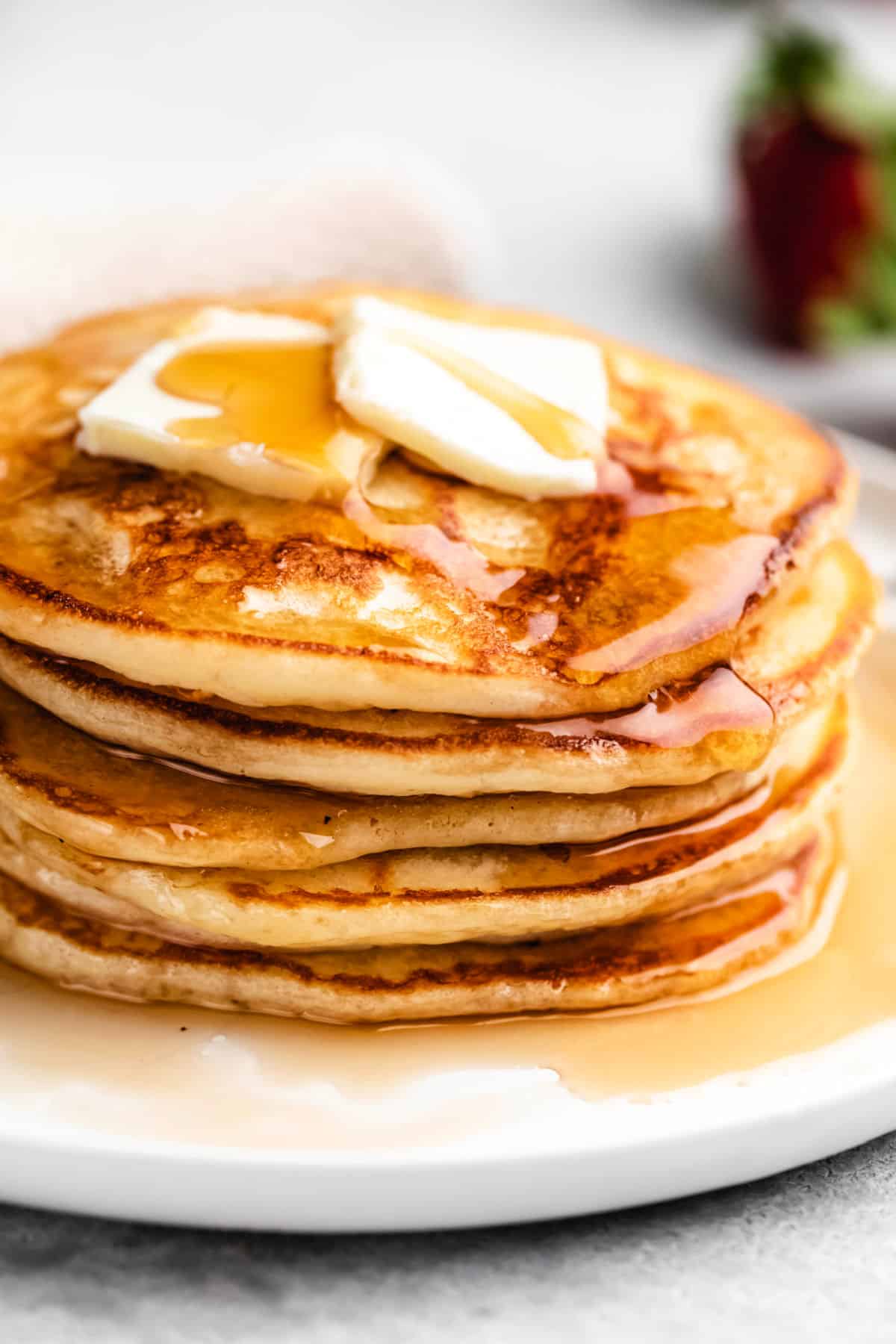 Close up photo of a stack of buttermilk pancakes with two pats of butter and syrup on top.