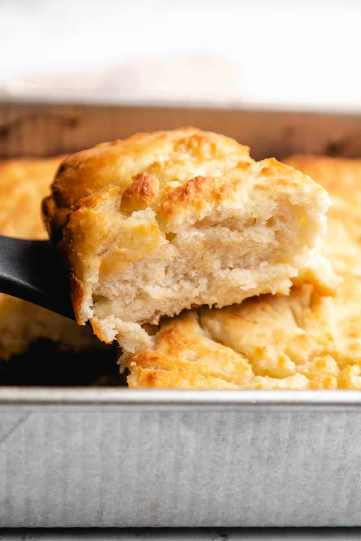 A spatula lifting up a butter swim biscuit from the pan.