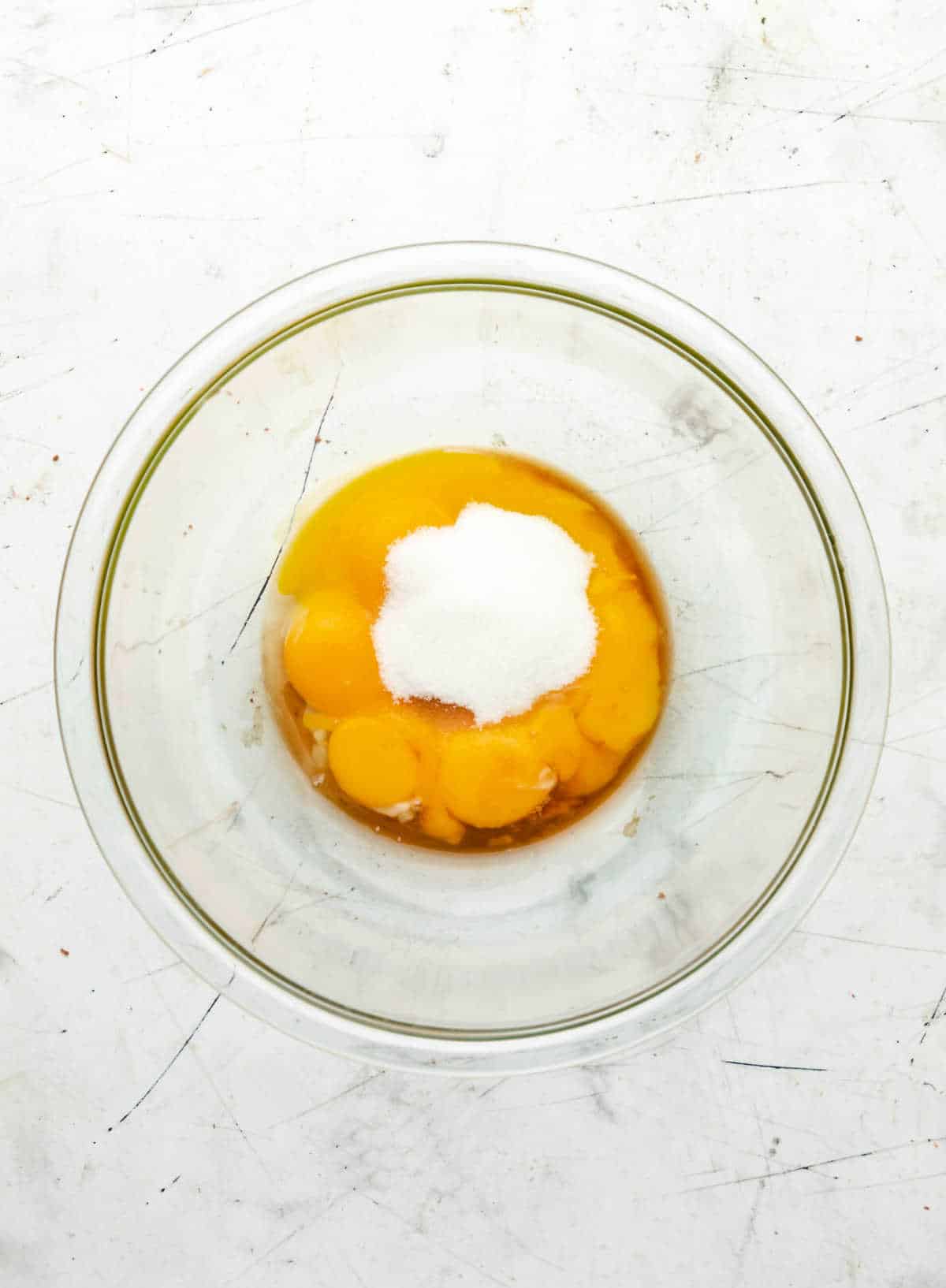 Egg yolks sugar and vanilla extract in a glass mixing bowl. 