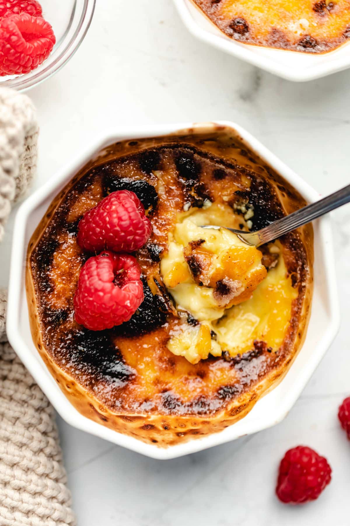 A spoon scooping up a bite of creme bruhlee from a ramekin.