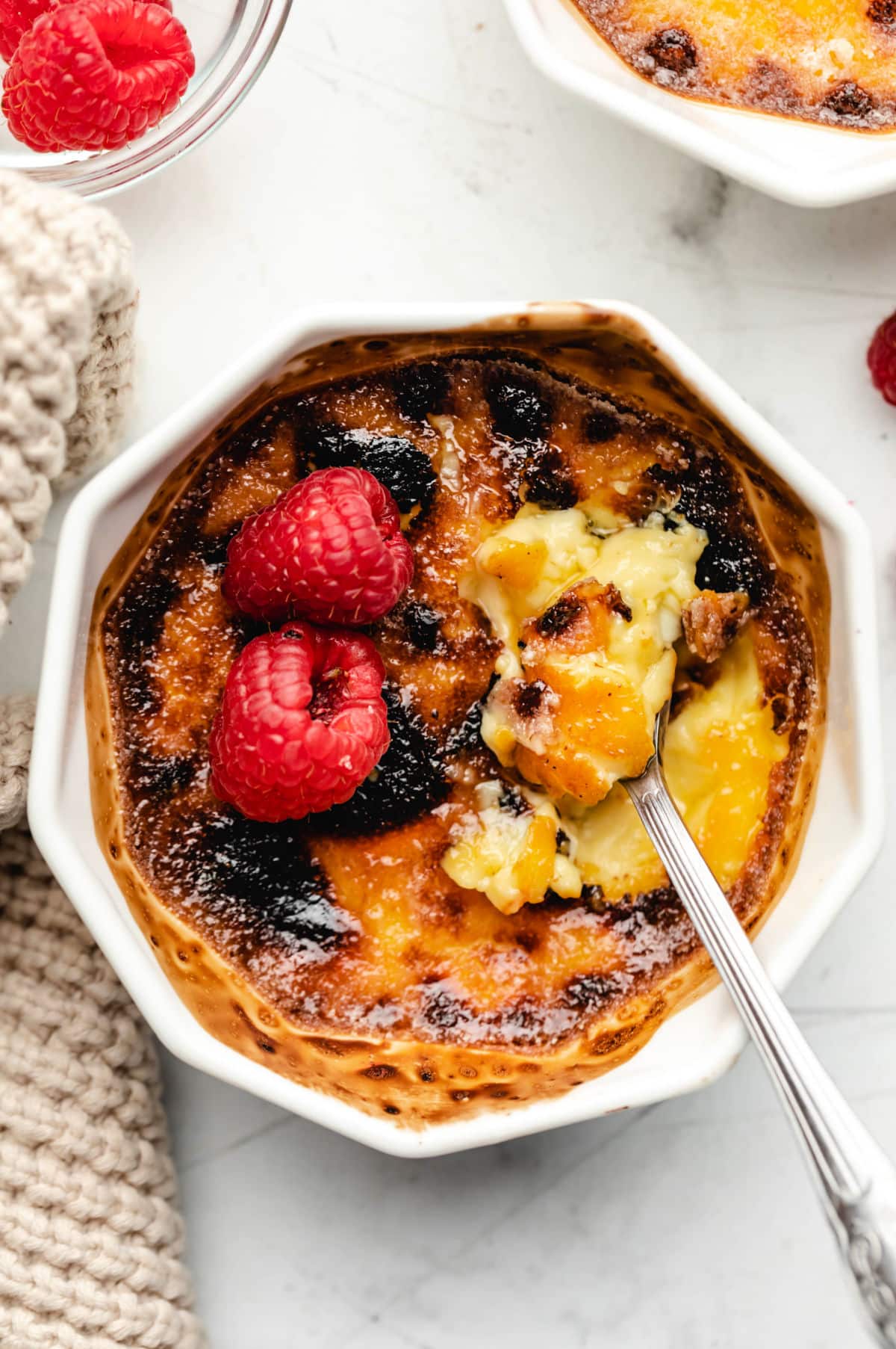 A ramekin with creme bruhlee with two raspberries on top. 