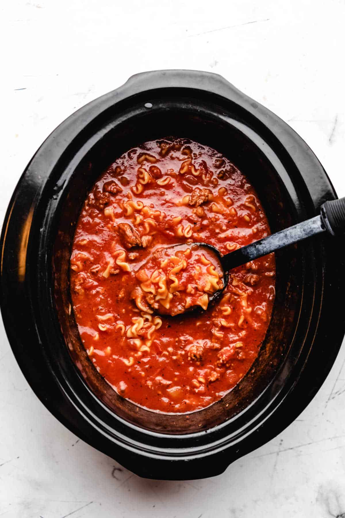 A black spoon stirring lasagna soup in a slow cooker. 