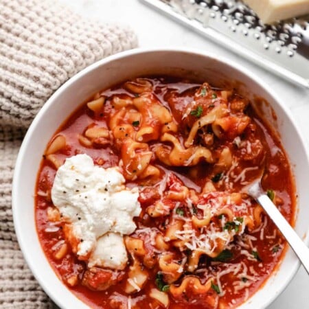 A block of parmesan on a hand grater next to a bowl of crock pot lasagna soup.