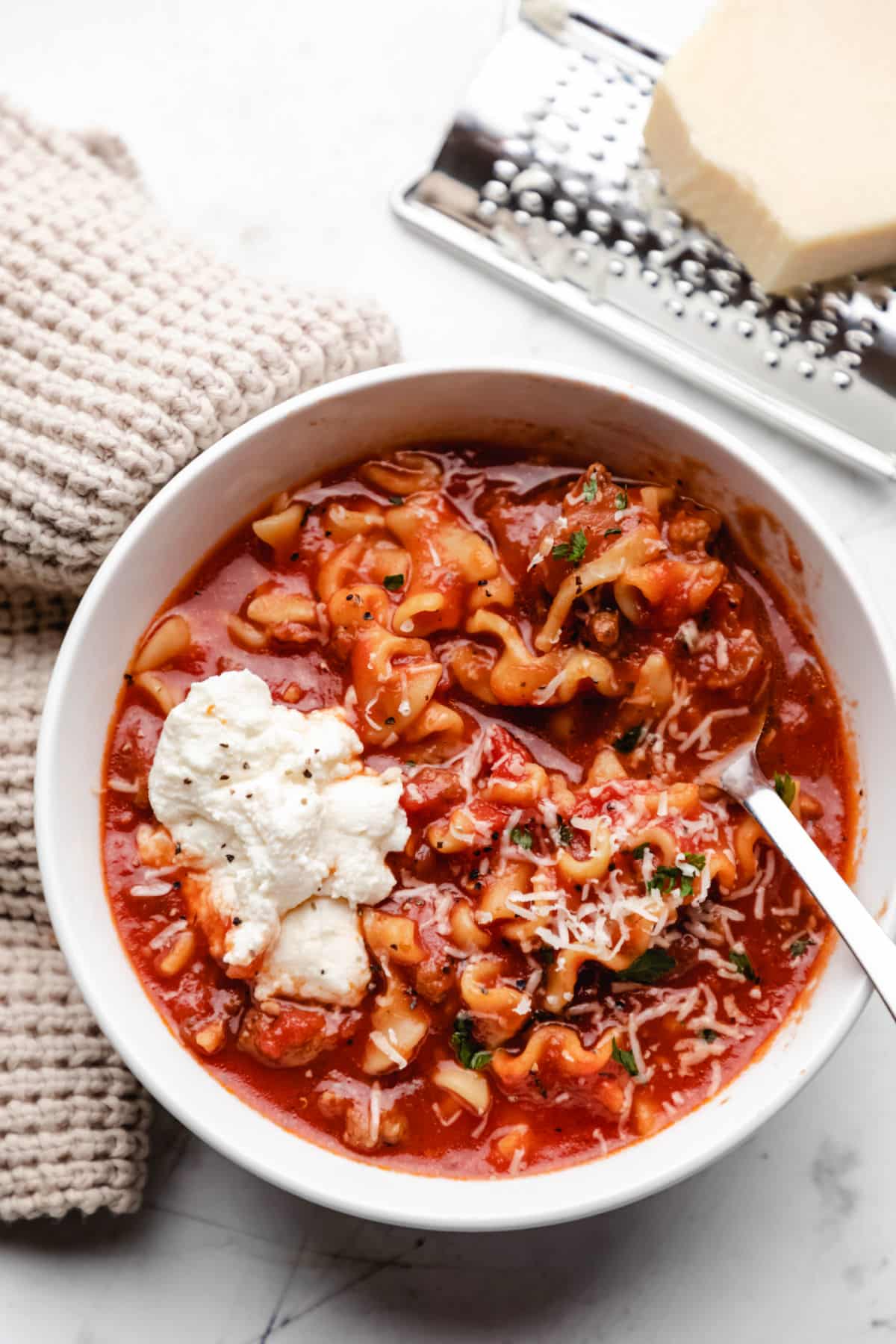 A block of parmesan on a hand grater next to a bowl of crock pot lasagna soup. 