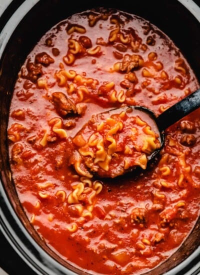 A black spoon scooping up lasagna soup from a crock pot.