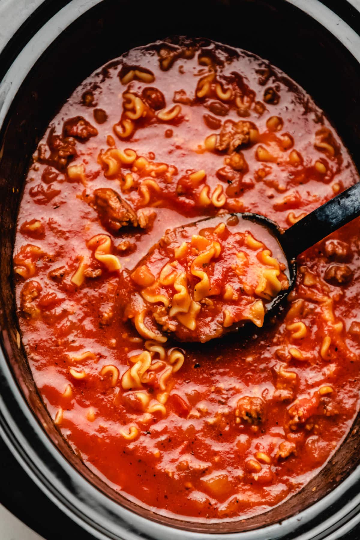 A black spoon scooping up lasagna soup from a crock pot.