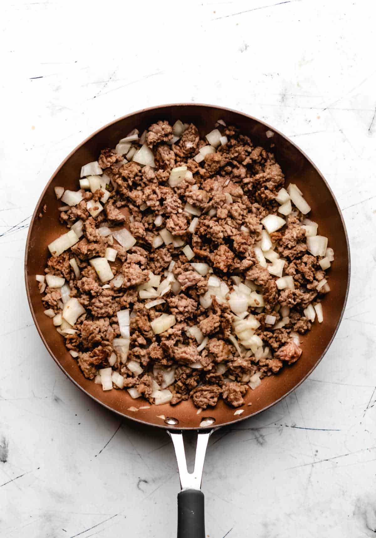 Sauteed onion and browned Italian sausage in a skillet. 