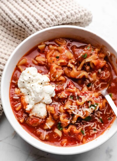 Close up photo of a white bowl of lasagna soup with a dollop of ricotta cheese on it.