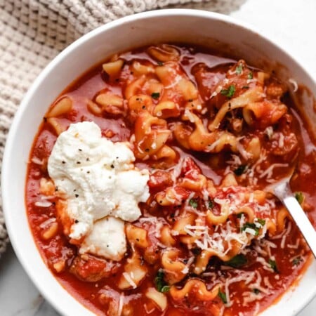 Close up photo of a white bowl of lasagna soup with a dollop of ricotta cheese on it.