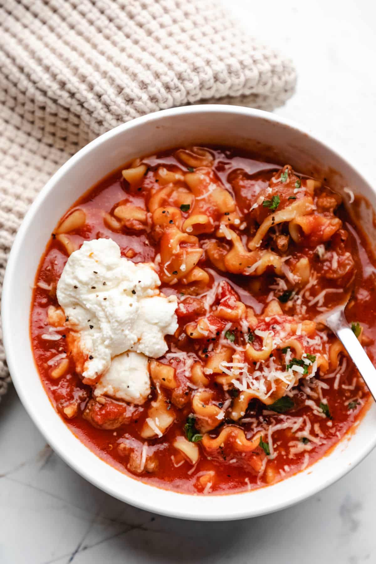 Close up photo of a white bowl of lasagna soup with a dollop of ricotta cheese on it.