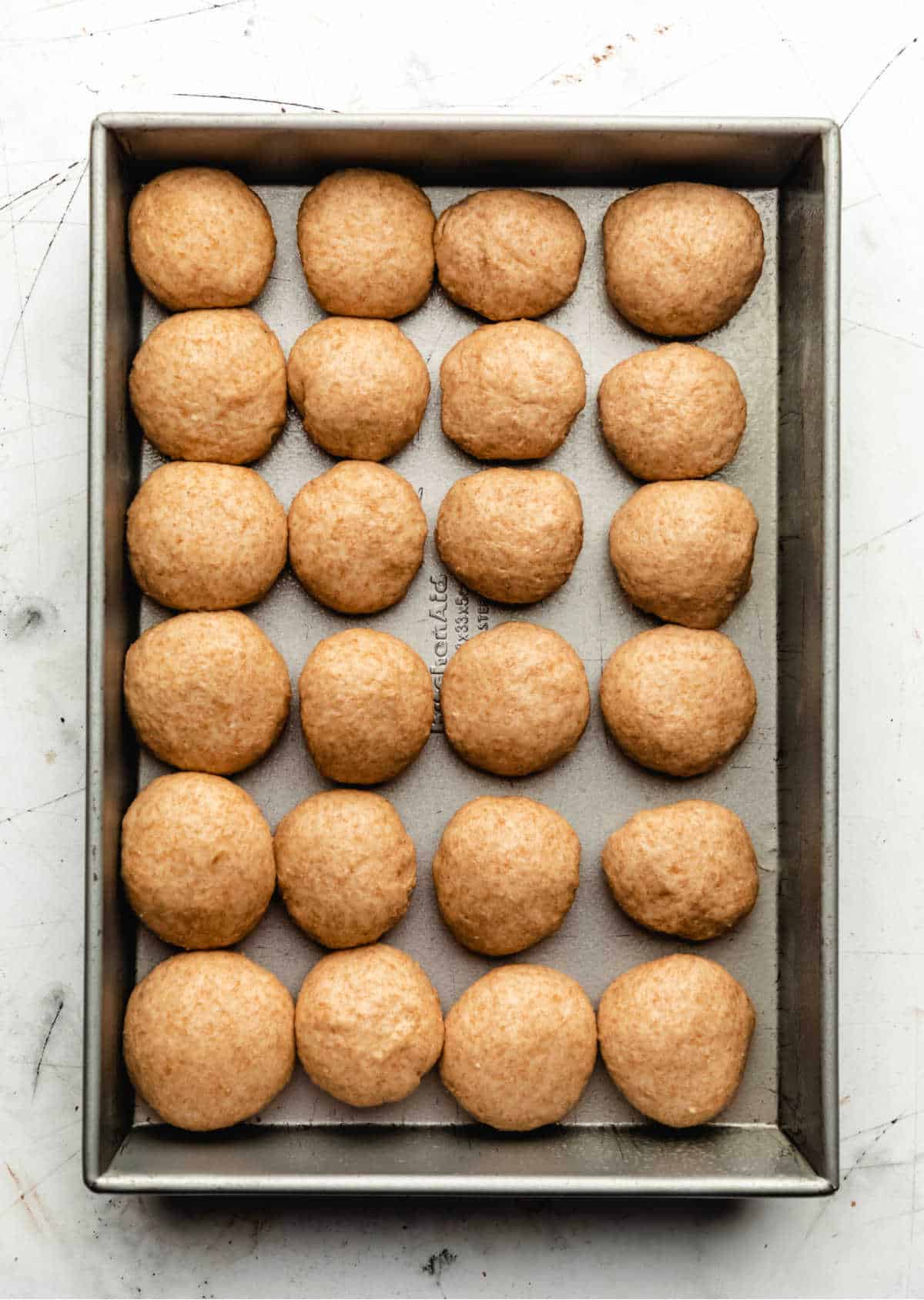 Twenty four unrisen rolls in a baking pan.