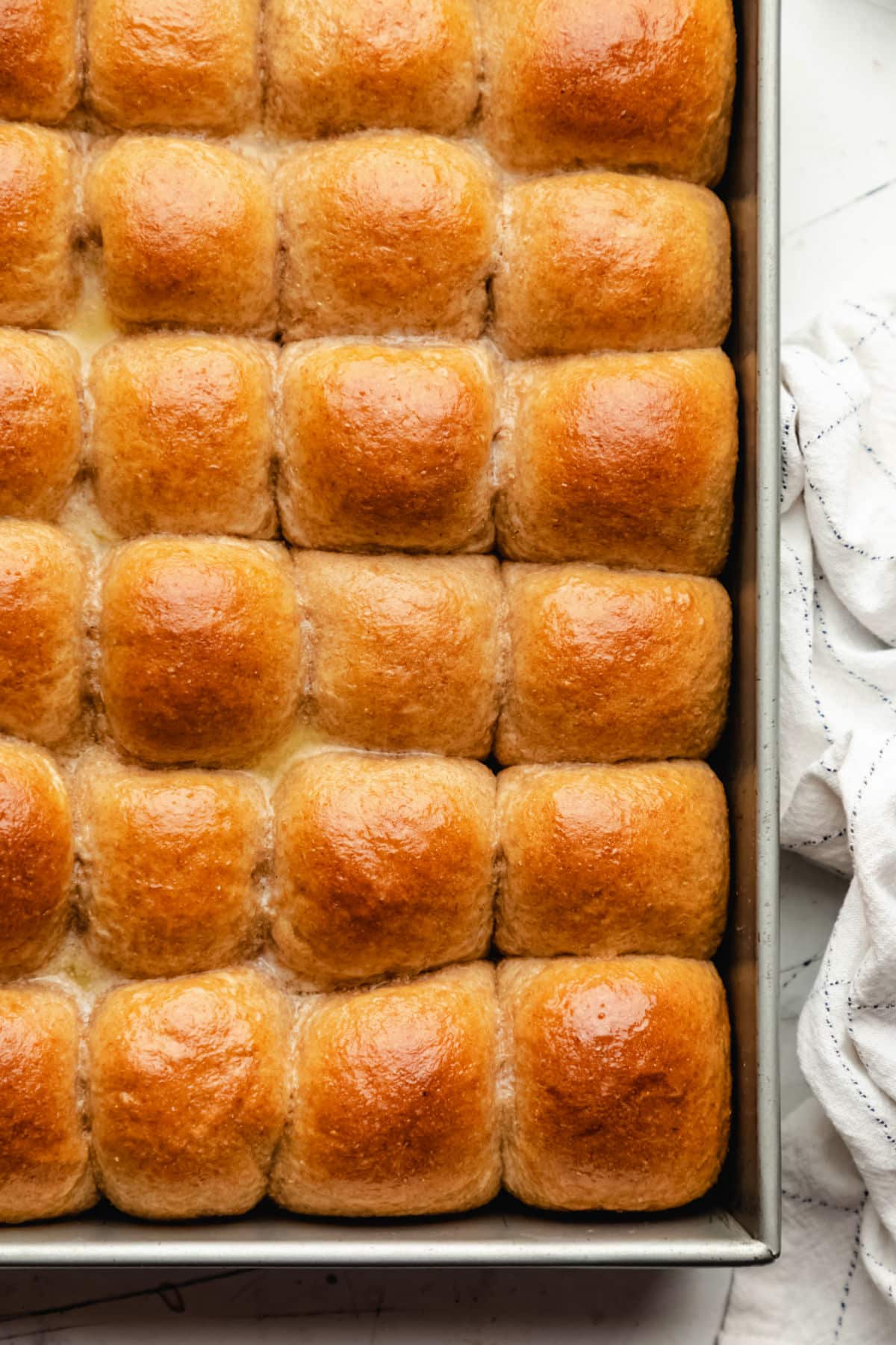 A pan of honey wheat rolls next to a kitchen linen.