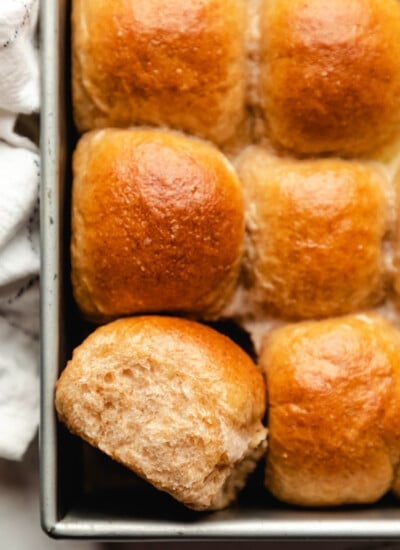 One whole wheat dinner roll on its side in a pan of rolls.