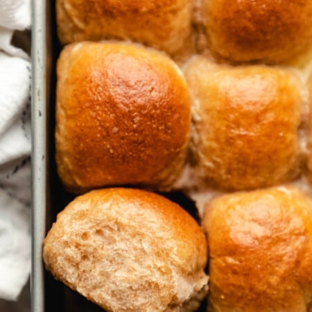 One whole wheat dinner roll on its side in a pan of rolls.