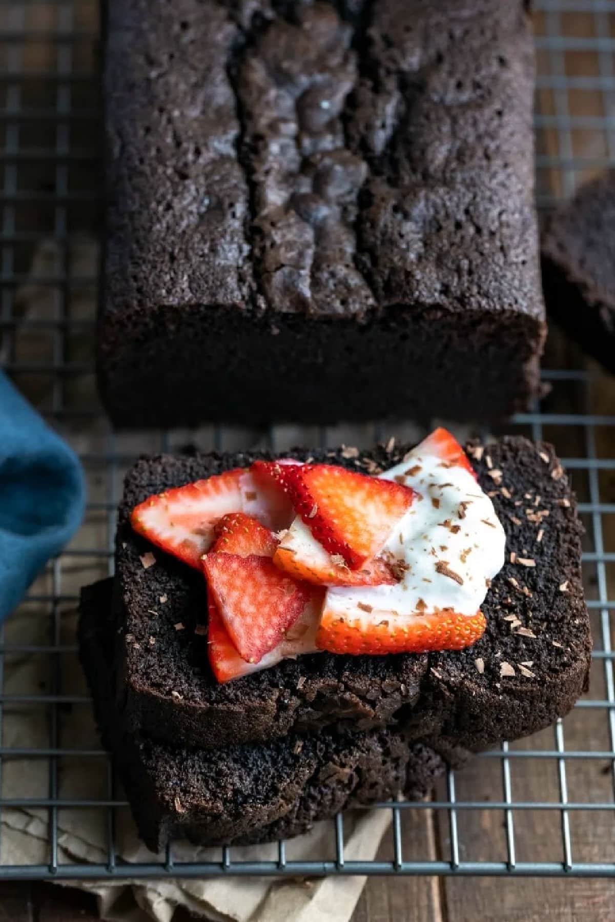 Two pieces of chocolate pound cake topped with strawberries and whipped cream on a wire rack.