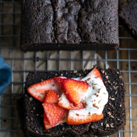 A piece of chocolate pound cake topped with sliced strawberries and whipped cream.