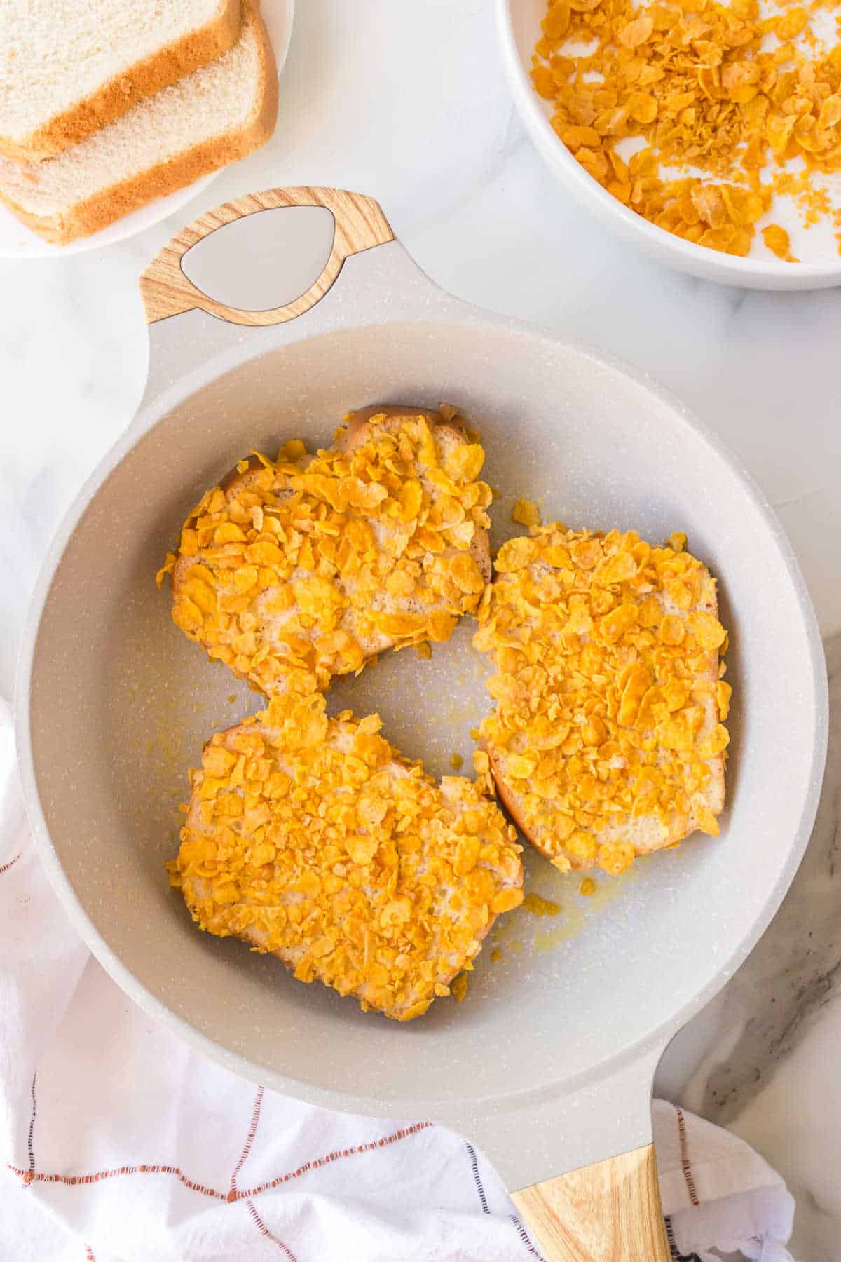 Three pieces of cornflake French toast cooking in a skillet. 