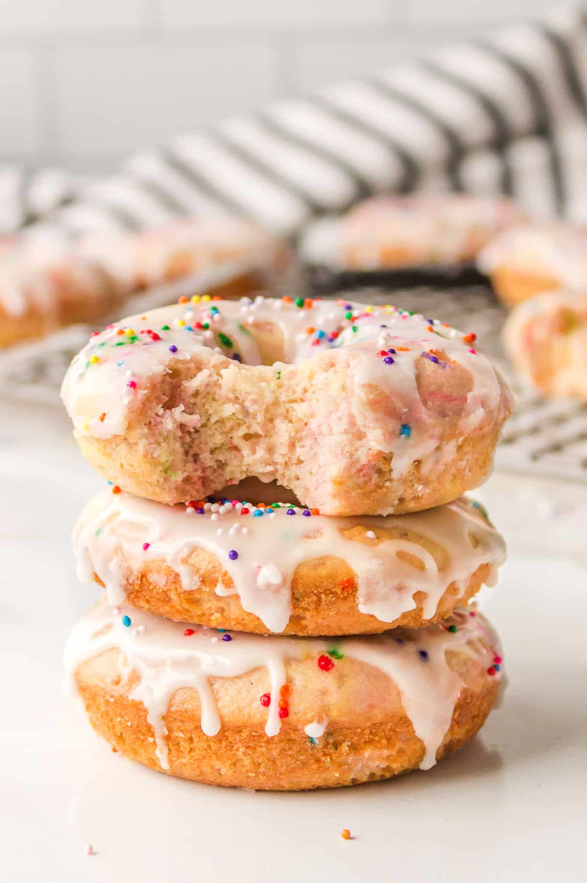 Three baked funfetti donuts with the top donut with a bite out of it. 