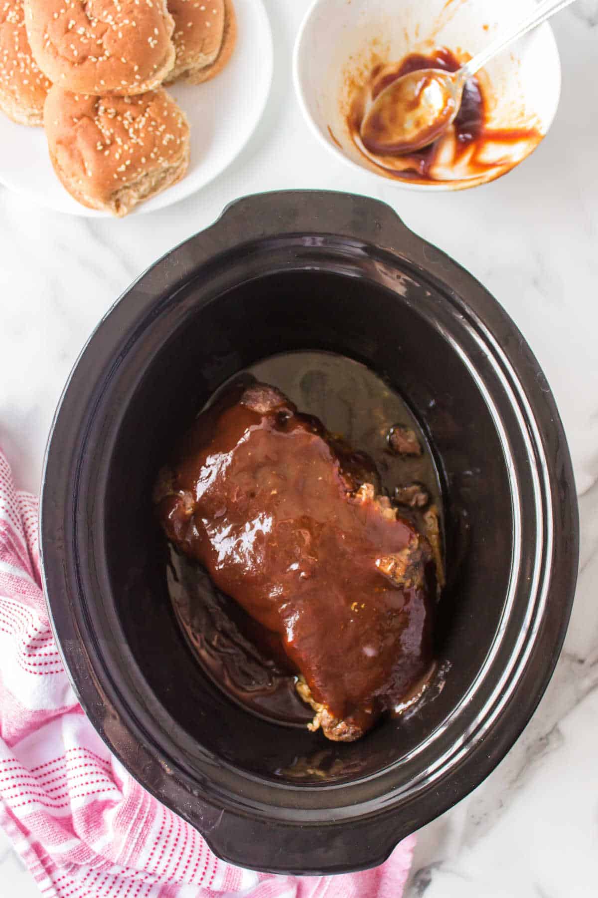 A brisket topped with barbecue sauce in a slow cooker. 