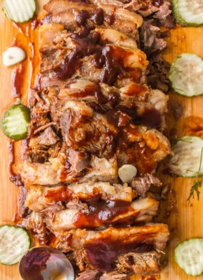 Sliced brisket on a wooden cutting board topped with sauce.