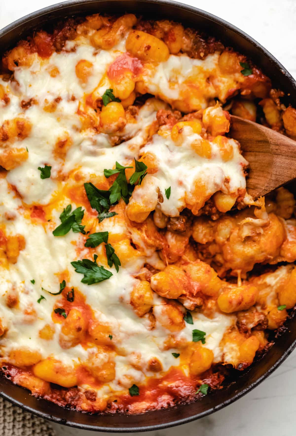 A wooden spoon scooping up baked gnocchi. 