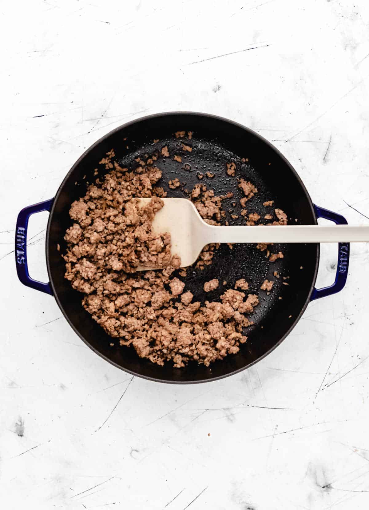 A spatula stirring browning Italian sausage.