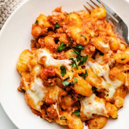 A cream dish with baked gnocchi and a fork on it.