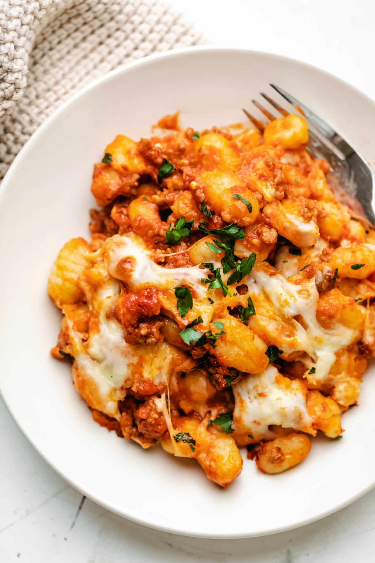 A cream dish with baked gnocchi and a fork on it.