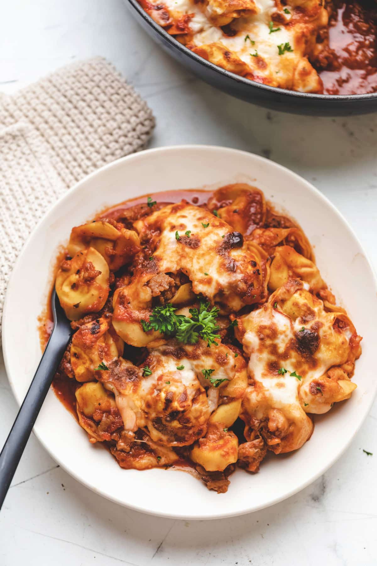 A plate of baked tortellini topped with fresh parsley. 