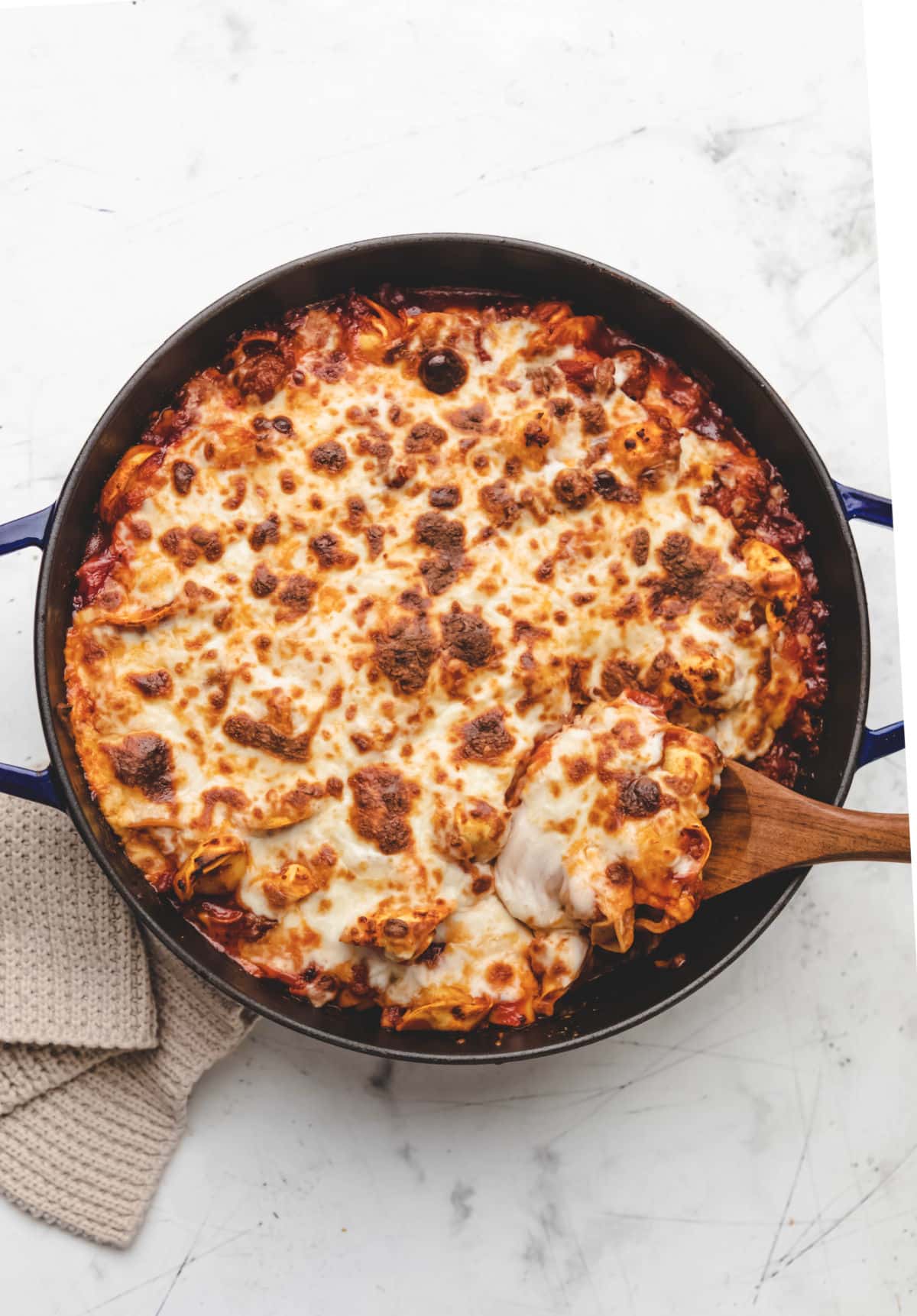 A wooden spoon in a skillet of baked tortellini. 