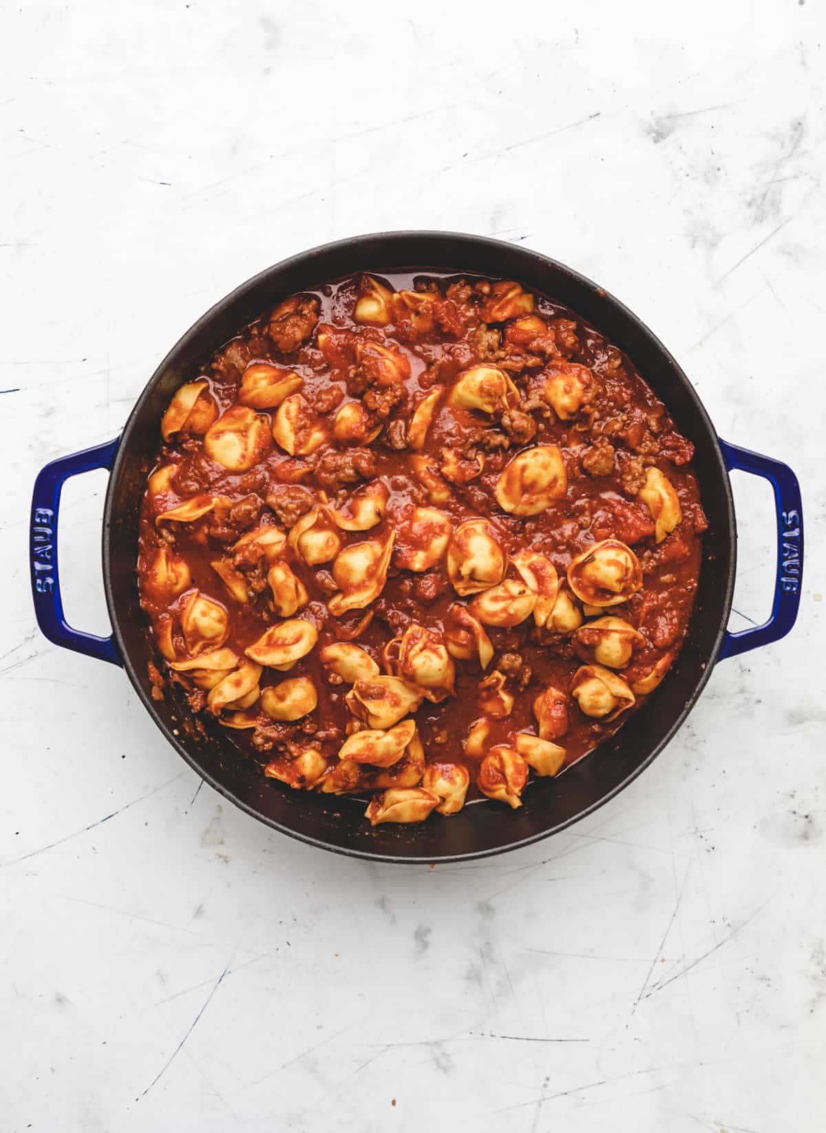 Uncooked cheese tortellini in sauce in a pan.