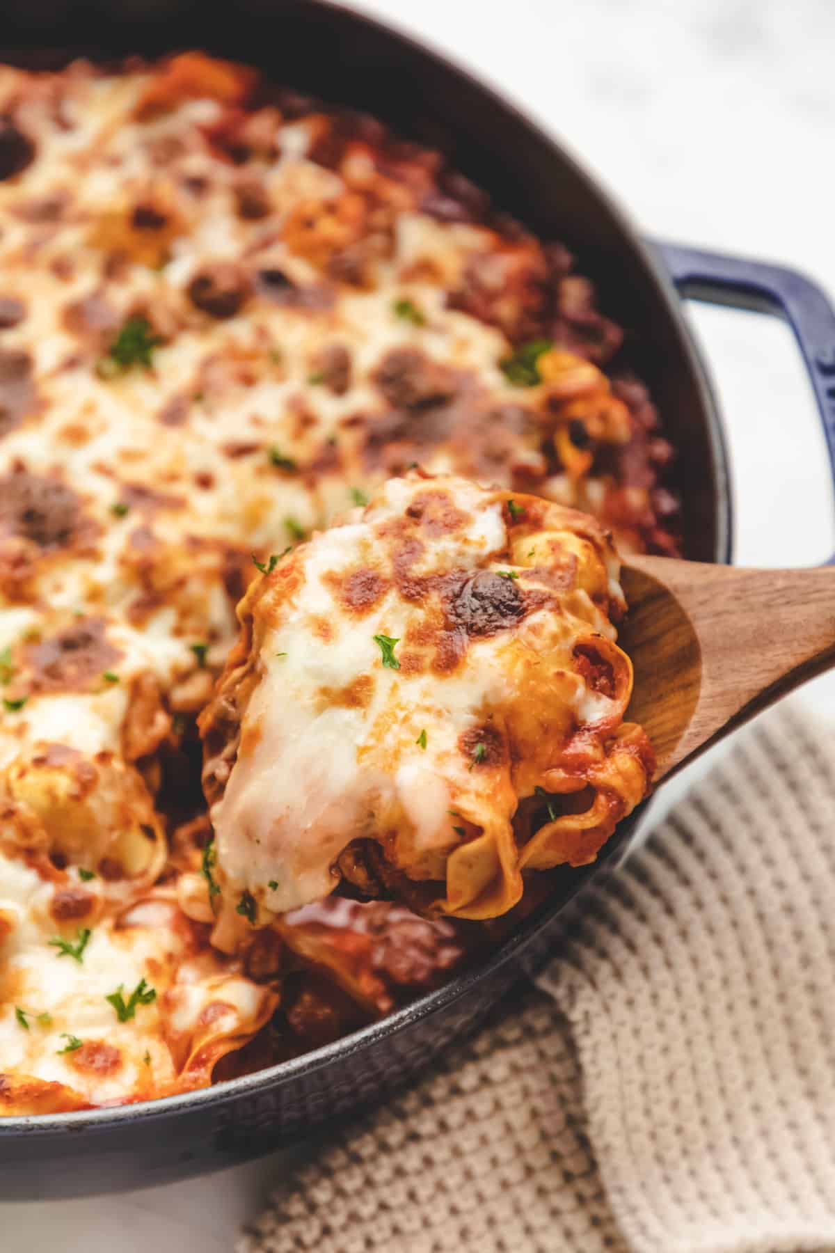 A wooden spoon holding up a scoop of baked tortellini. 