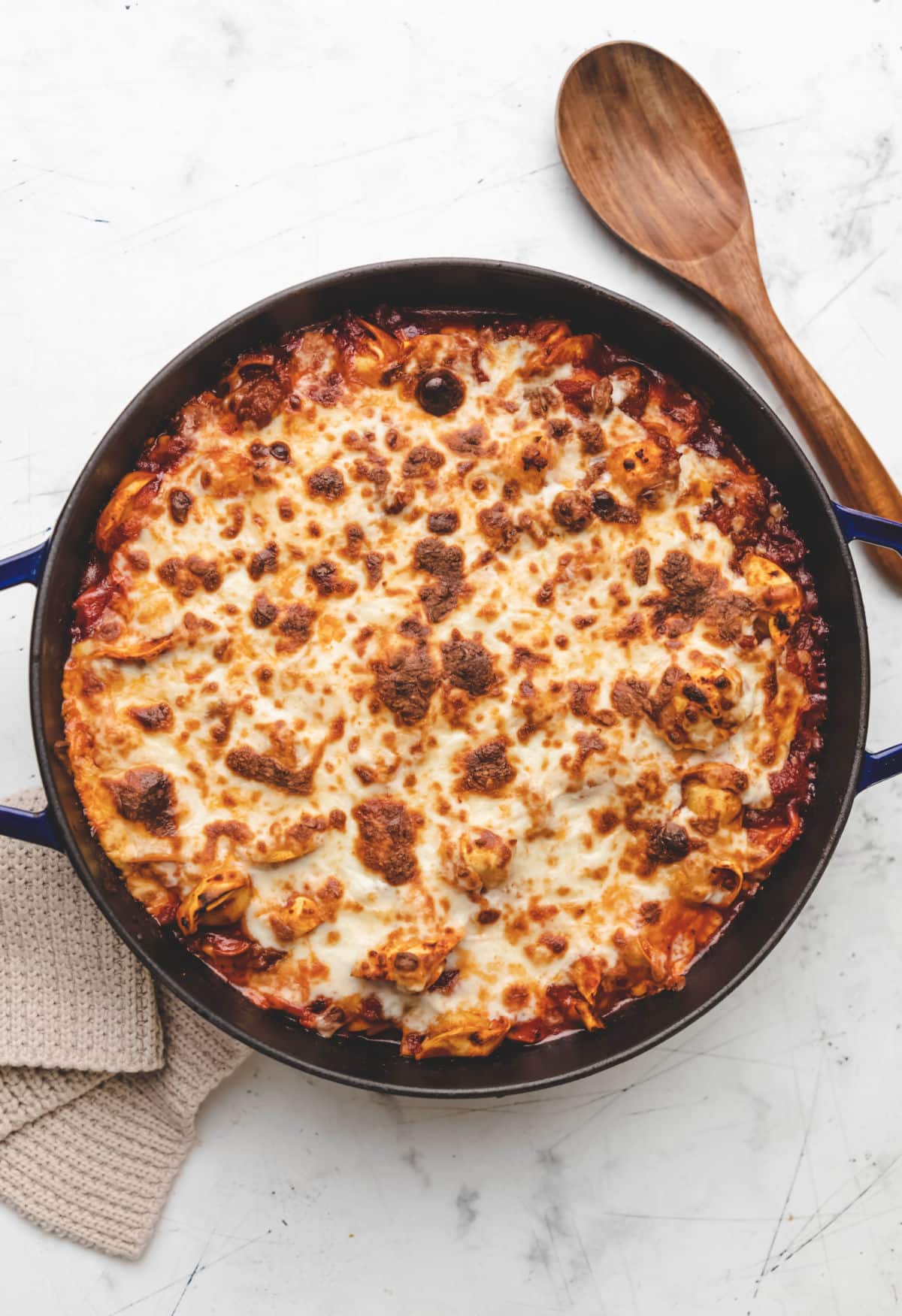 A pan of baked tortellini next to a wooden spoon. 